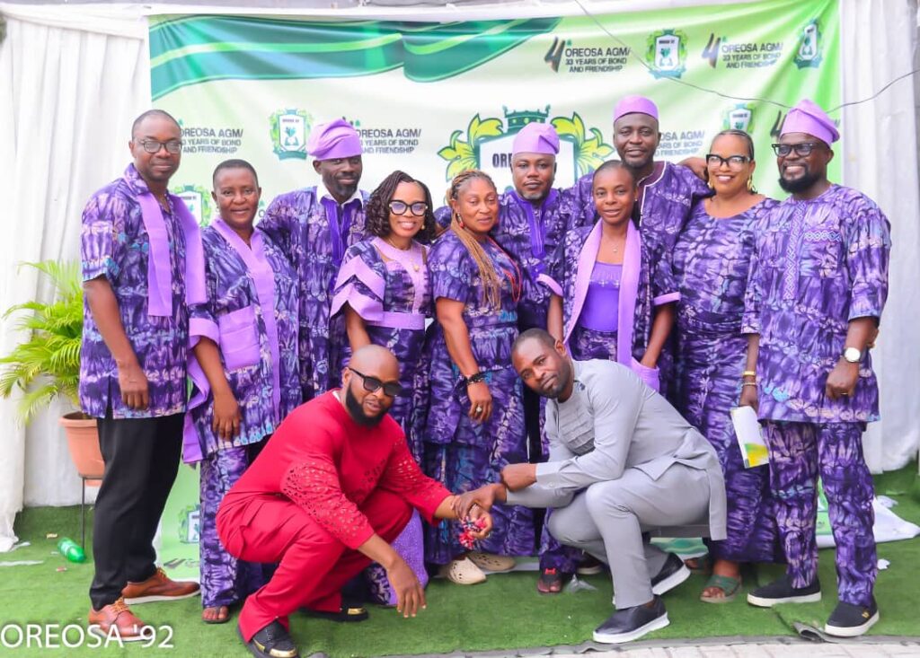 Group of OREOSA92 members in matching purple traditional attire posing together in front of the association's AGM backdrop